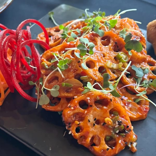 Spicy lotus root slices garnished with microgreens and red pickled vegetables on a dark plate.