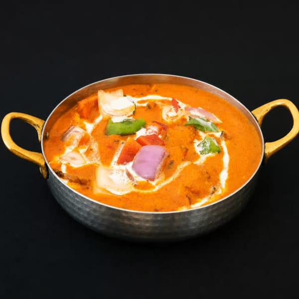 A vibrant orange curry with colorful bell peppers and onions, garnished with cream, in a metal pot.